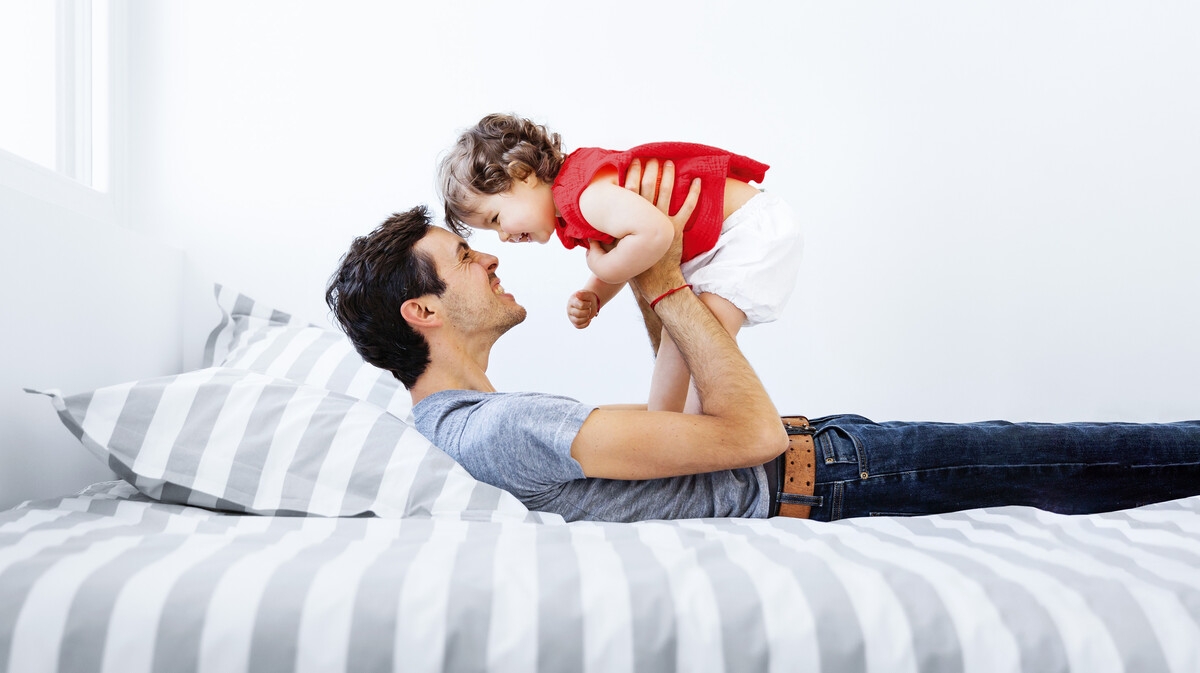 Laughing father lies on his back and lifts up laughing child